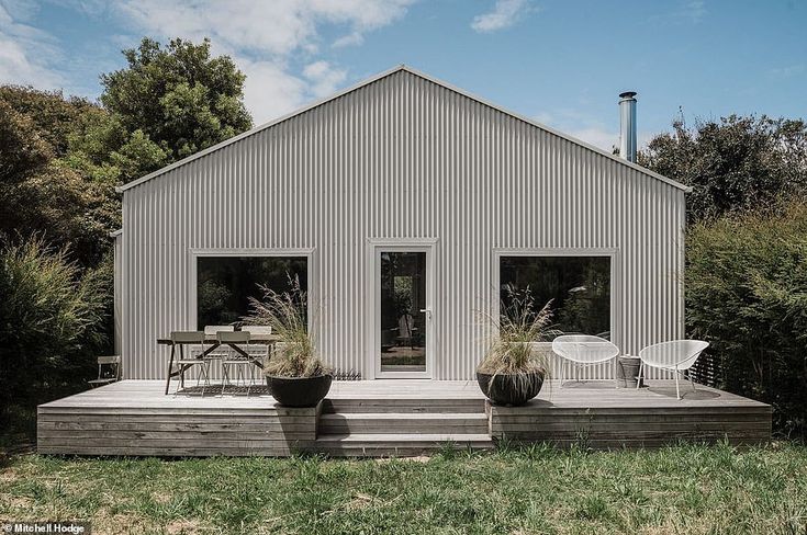 a house that has some plants in front of it and two chairs on the porch