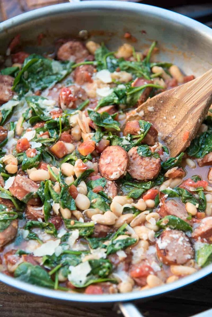 sausage, beans and spinach in a pan with a wooden spoon