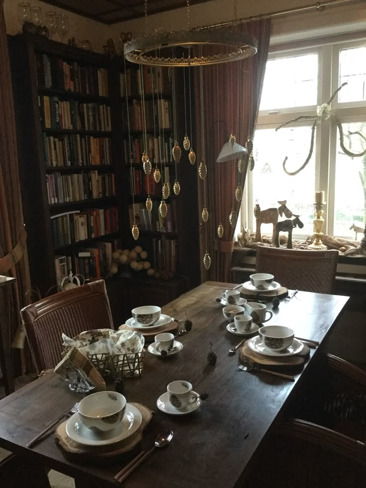 a dining room table with plates and cups on it in front of a bookshelf