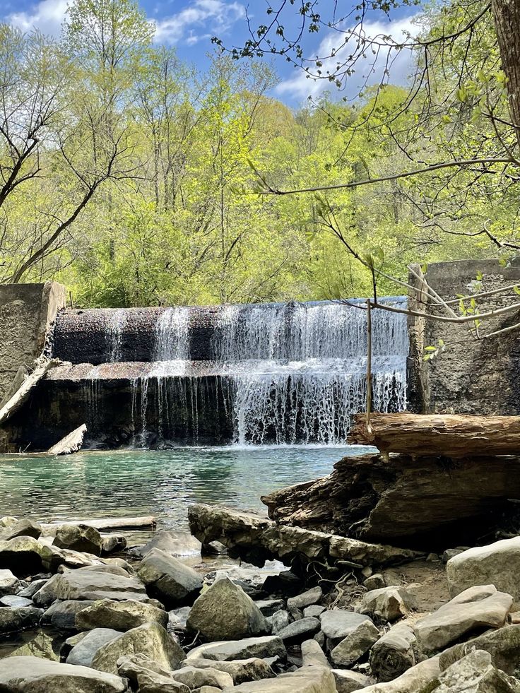 a large waterfall in the middle of a river surrounded by rocks and trees on a sunny day