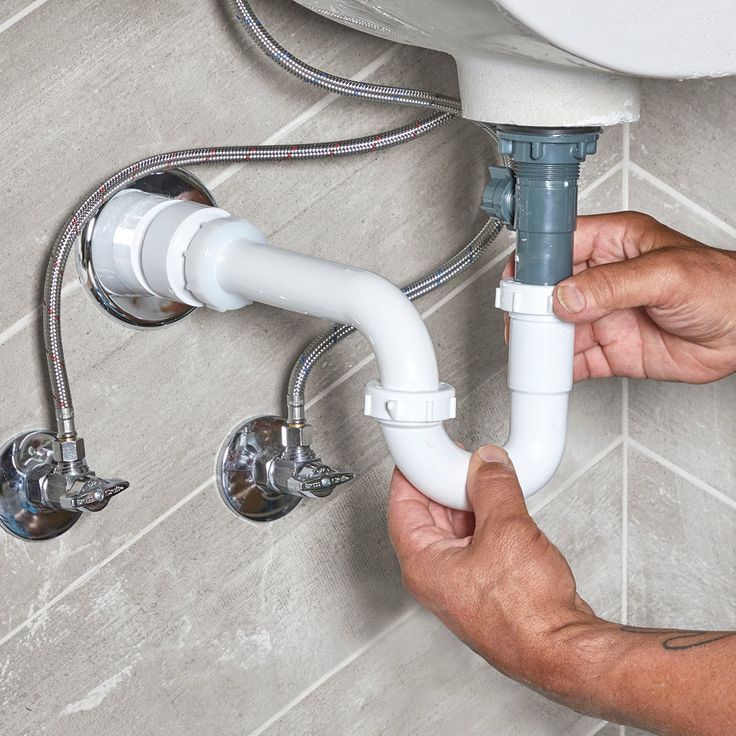 a person fixing a toilet with two hoses attached to the wall next to it