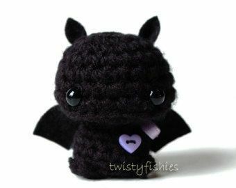 a small black bat stuffed animal sitting on top of a white table next to a purple heart