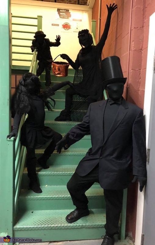 three people dressed in black are climbing the stairs with their hands up and one is wearing a top hat