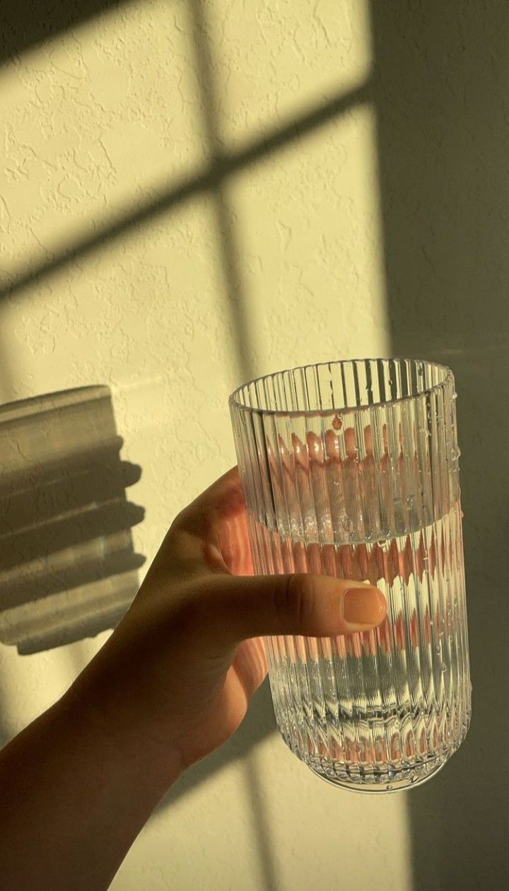 a person holding a glass in front of a window with the sun shining through it