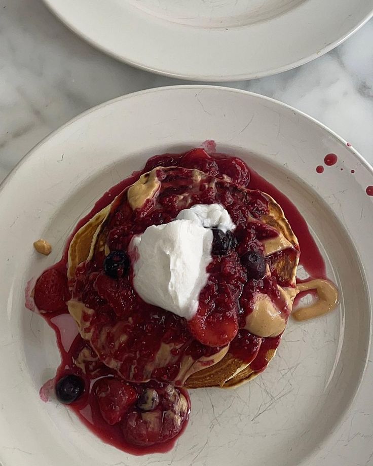 two white plates topped with pancakes covered in syrup and whipped cream, sitting on a marble table