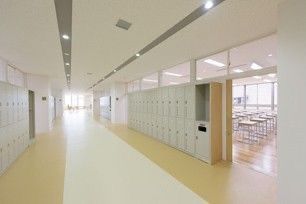 an empty hallway with lockers and tables in the center, leading to another room