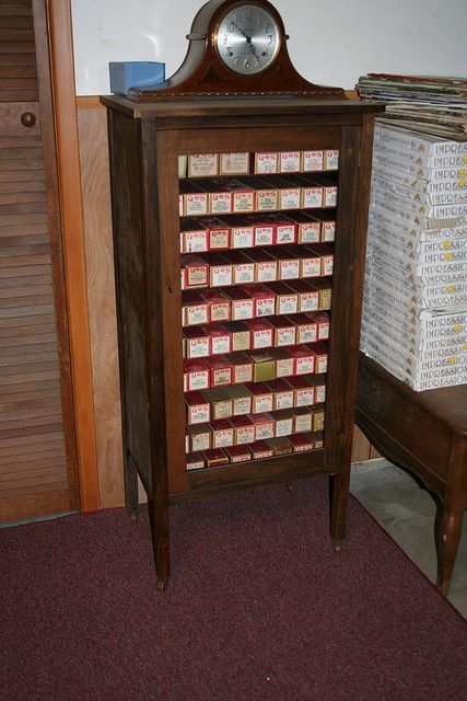 an old wooden clock sitting on top of a table next to a chair and bookshelf