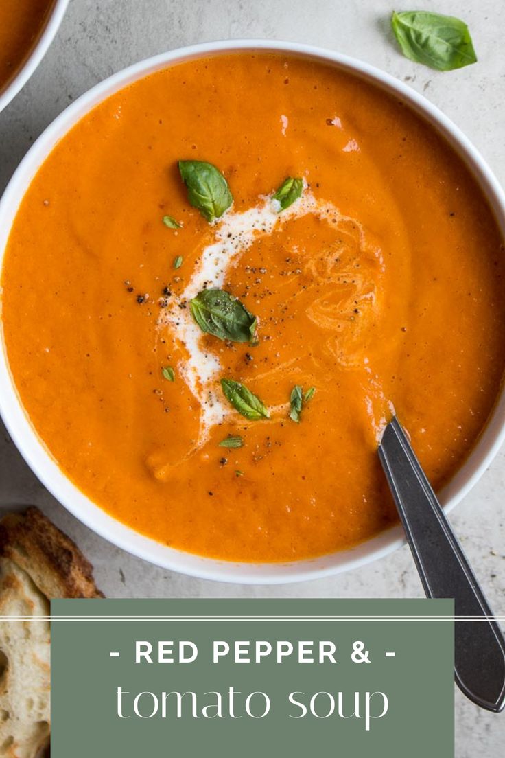 two bowls of red pepper and tomato soup with basil garnish on the side