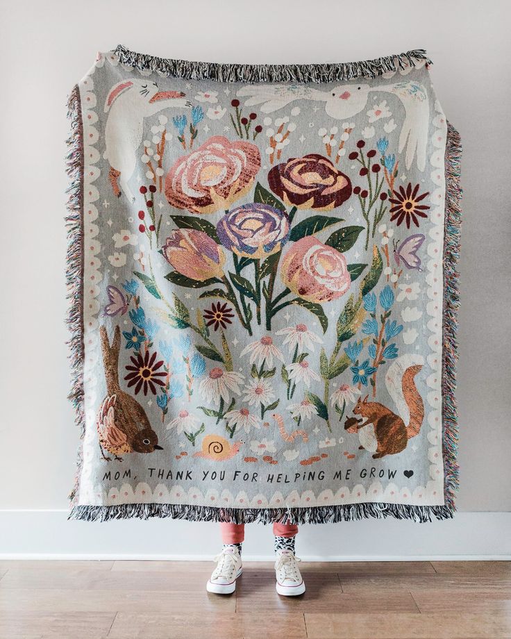 a woman standing in front of a white wall holding a blanket with flowers on it