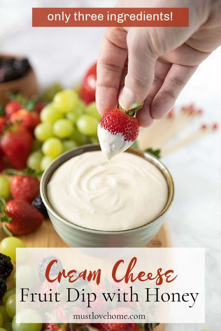 a hand dipping a strawberry into a bowl of cream cheese fruit dip with honey