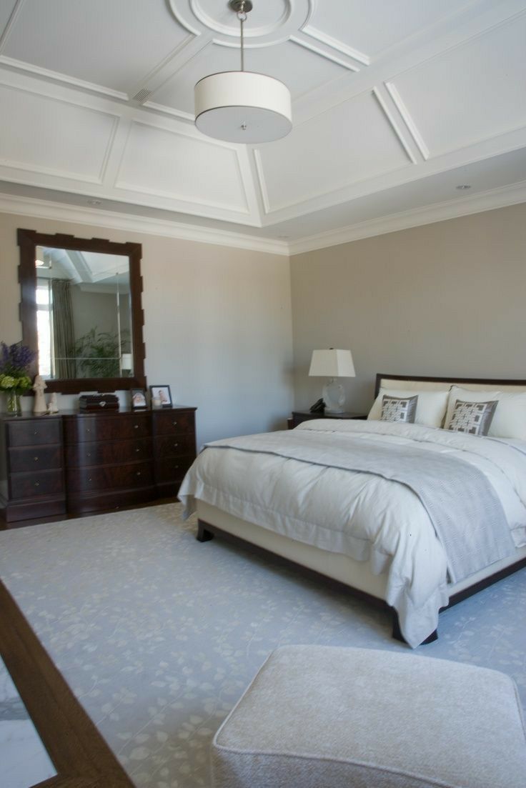 a bedroom with a bed, dresser and mirror on the wall next to an ottoman