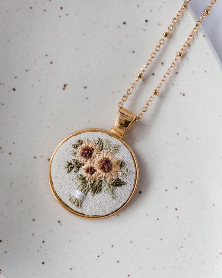 a necklace with flowers on it sitting on top of a white table next to a gold chain