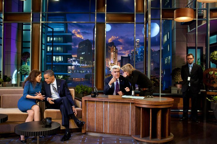 three people sitting on couches in front of large windows with city lights behind them