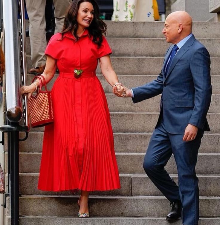 a woman in a red dress holding hands with a man in a blue suit