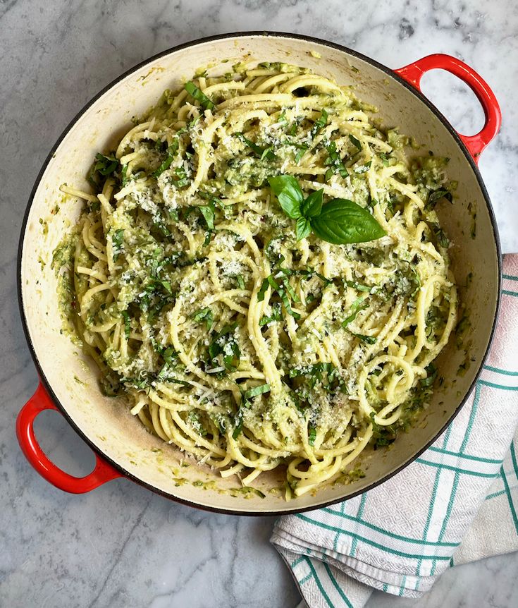 a red pot filled with pasta and pesto on top of a marble countertop