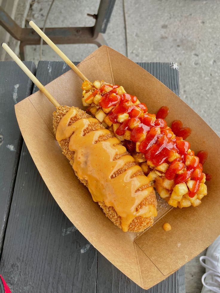 a hot dog covered in ketchup and toppings on a wooden table outdoors