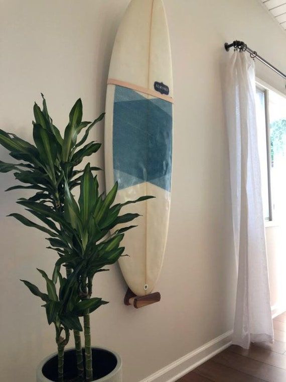 a surfboard hanging on the wall next to a potted plant in a room