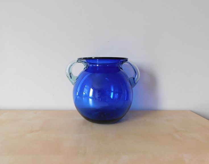 a blue glass vase sitting on top of a wooden table next to a white wall