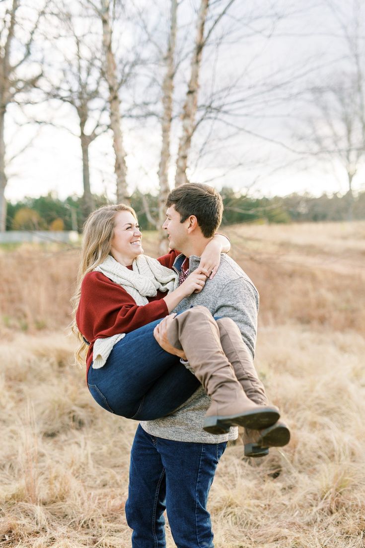 a man carrying a woman on his back in an open field with tall grass and trees