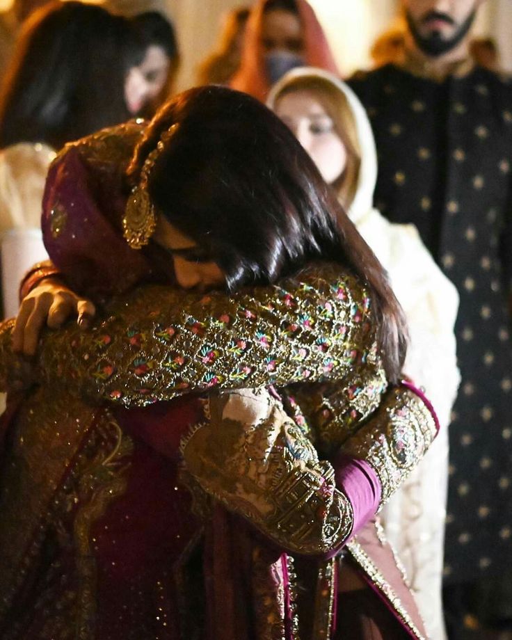 a woman in a red and gold dress hugging another woman with other people behind her