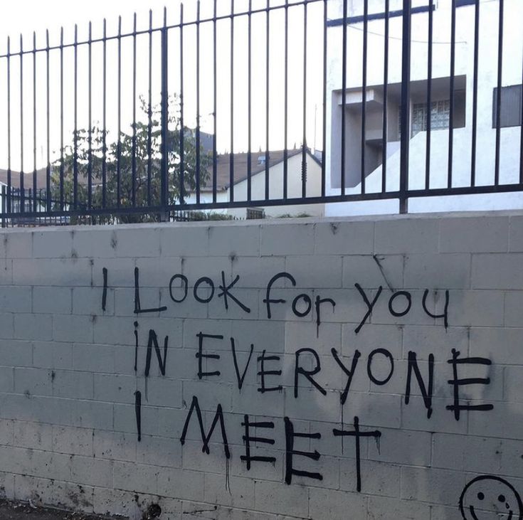 graffiti written on the side of a white brick wall near a black fence and gate