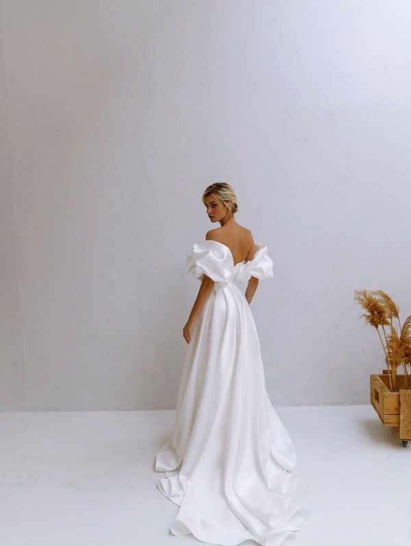 a woman in a white wedding dress standing next to a basket with wheat stalks on it