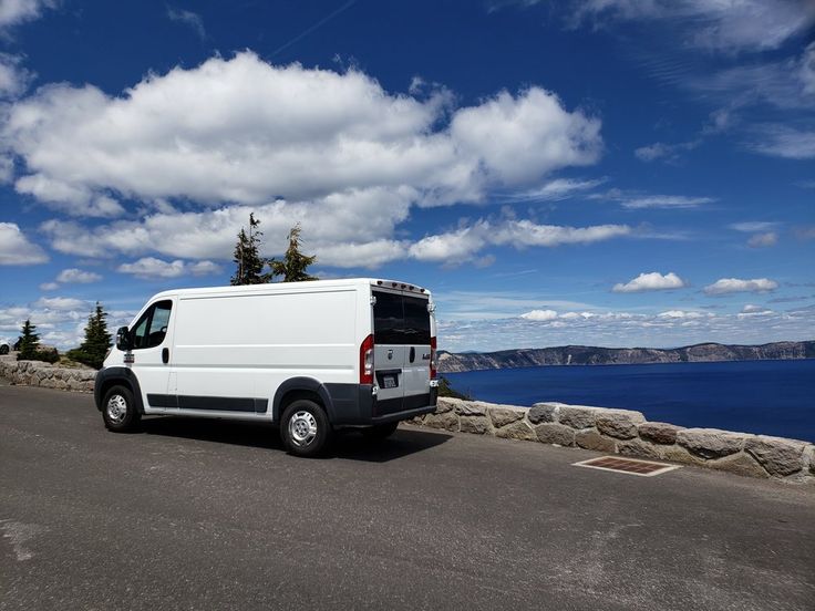 a white van parked on the side of a road next to some trees and water