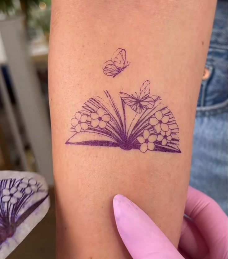 a woman's arm with a book and butterflies tattoo on it