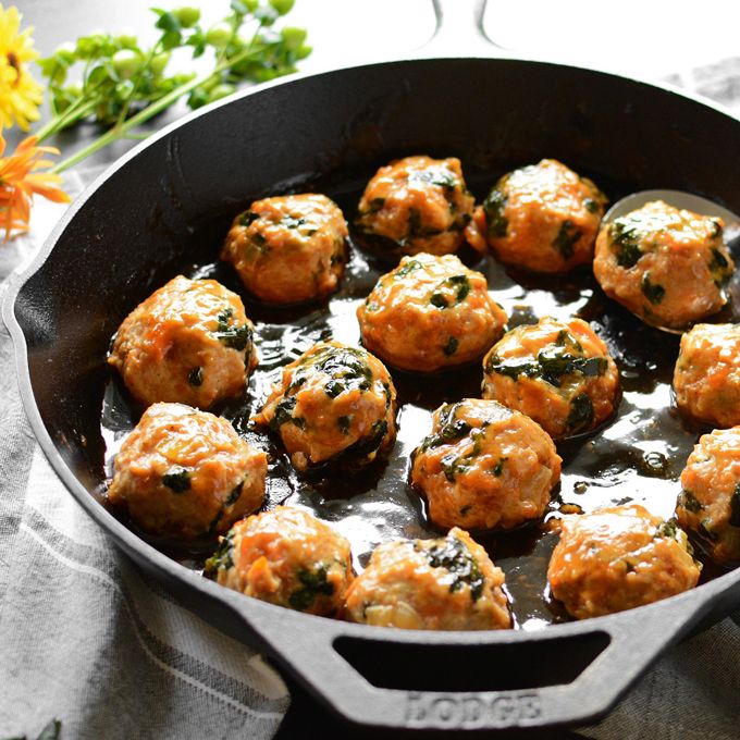 a pan filled with meatballs and sauce on top of a table next to flowers