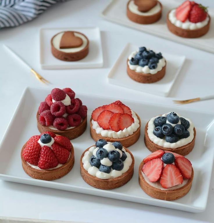 there are many small desserts on the plate and one is decorated with strawberries, blueberries, raspberries, and chocolate