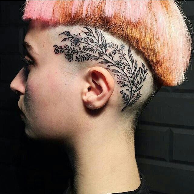 a woman with pink hair has a tattoo on her face and behind her ear is an image of leaves