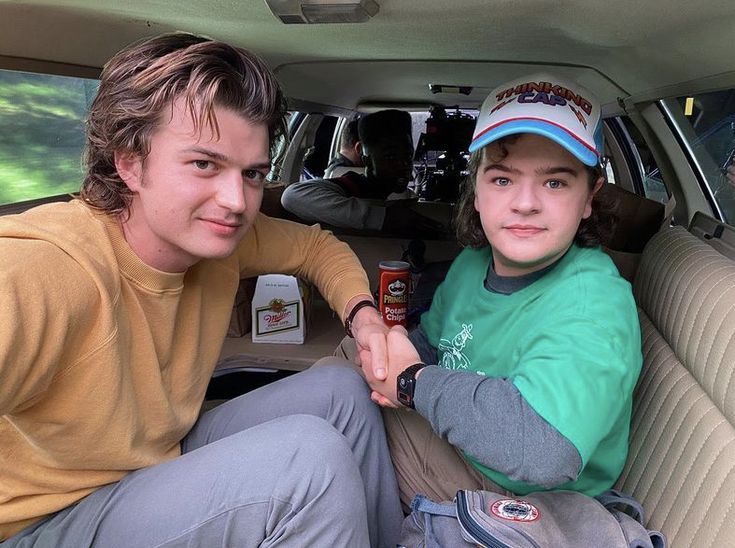 two people sitting in the back seat of a car, one is holding a beer