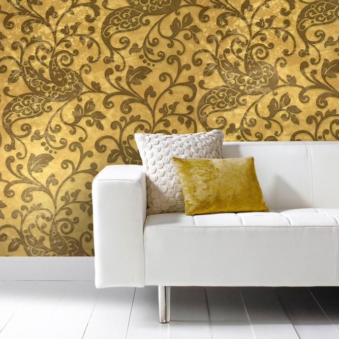 a white couch sitting in front of a wall with gold and brown designs on it