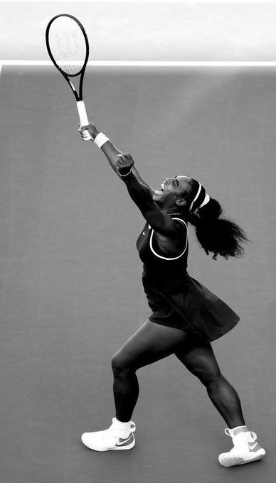 a female tennis player in black and white is serving the ball with her racket