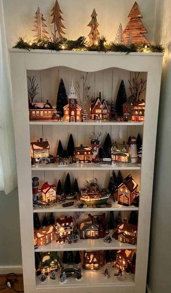 a white book shelf filled with lots of small christmas houses and lit up trees on top of it