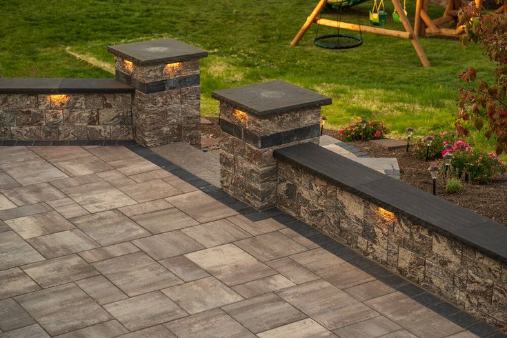 an outdoor patio with stone walls and lights on each side, surrounded by green grass