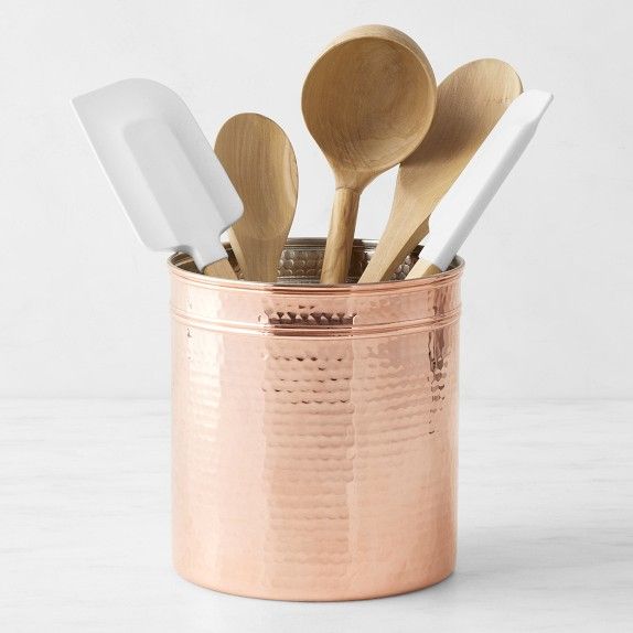 wooden spoons and utensils in a copper cup on a white table top