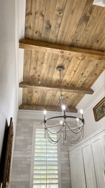 a chandelier hanging from the ceiling in a room with white walls and wooden beams