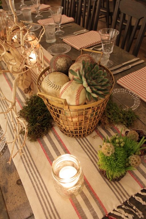 a table topped with a basket filled with baseballs and succulents next to candles