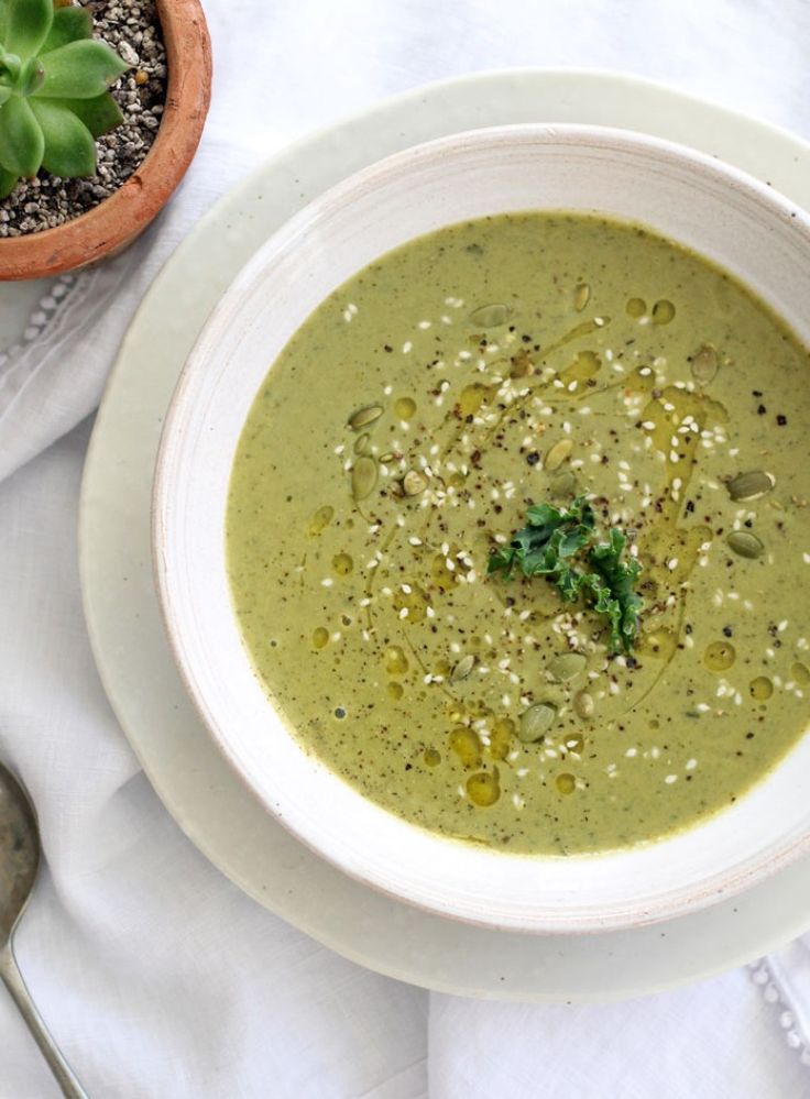 a white bowl filled with green soup next to a potted plant and spoons