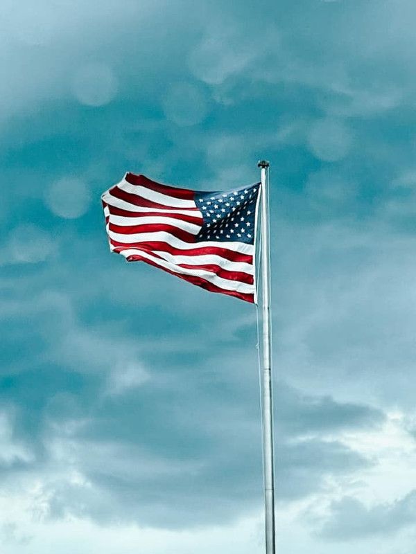 an american flag waving in the wind on a cloudy day with blue sky and clouds