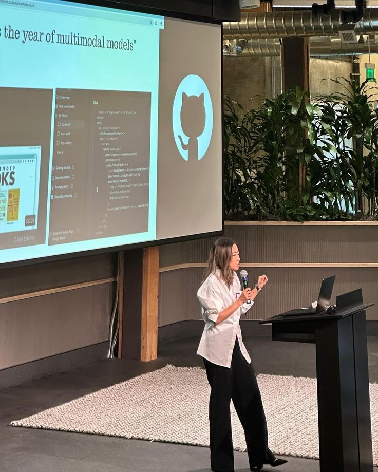 a woman standing at a podium in front of a projector screen giving a presentation