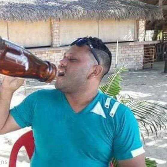 a man drinking from a beer bottle in front of a straw hut on the beach