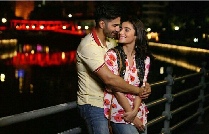 a man and woman standing next to each other on a bridge near water at night