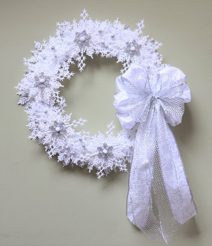 a snowflake wreath with white ribbon hanging on the wall next to it's side