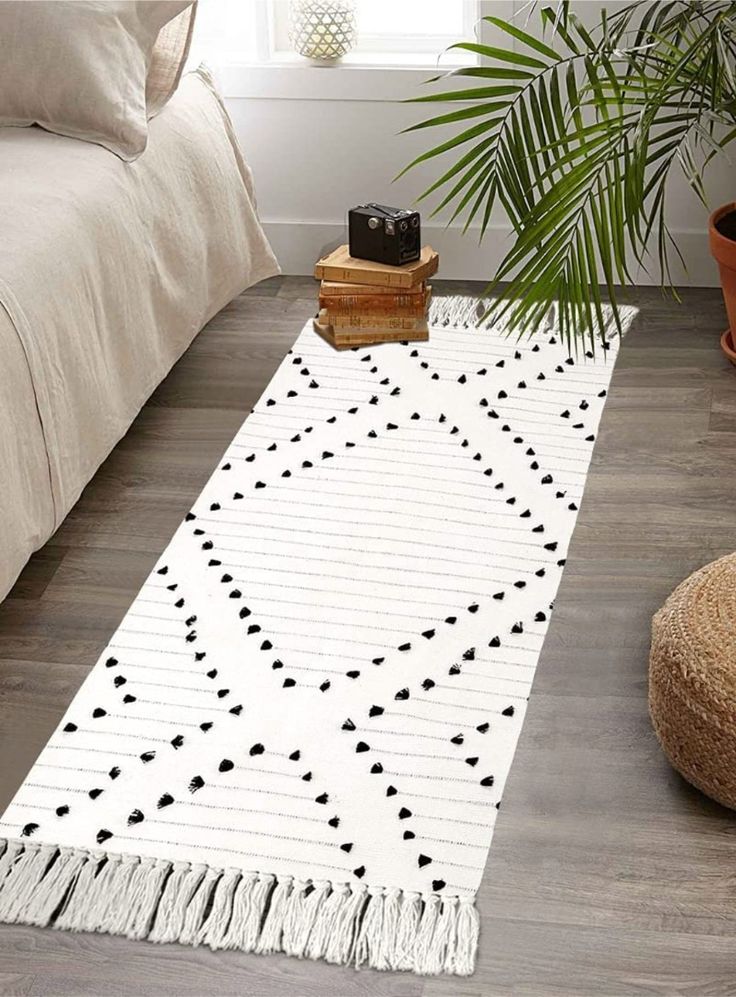 a white rug with black dots on it next to a bed and potted plant