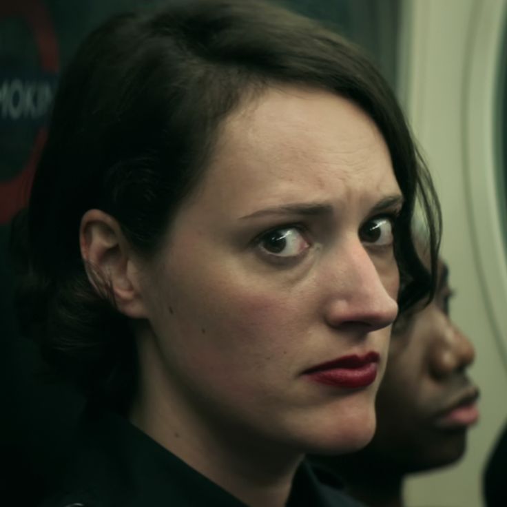 a woman looks at herself in the mirror while riding on a train or bus with another person behind her