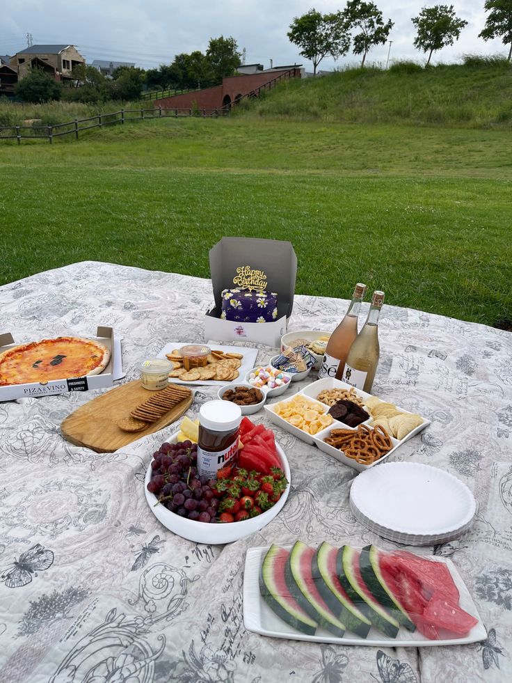 a picnic table with food and drinks on it in the middle of a grassy field