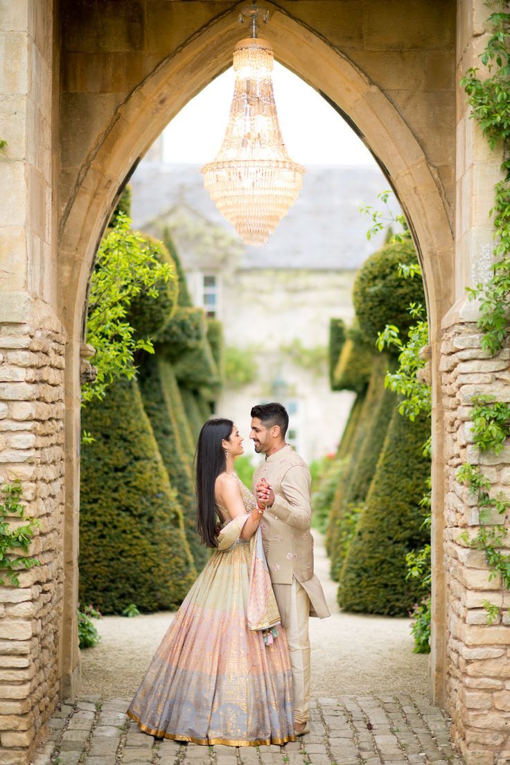 a man and woman standing in front of an archway with greenery on either side