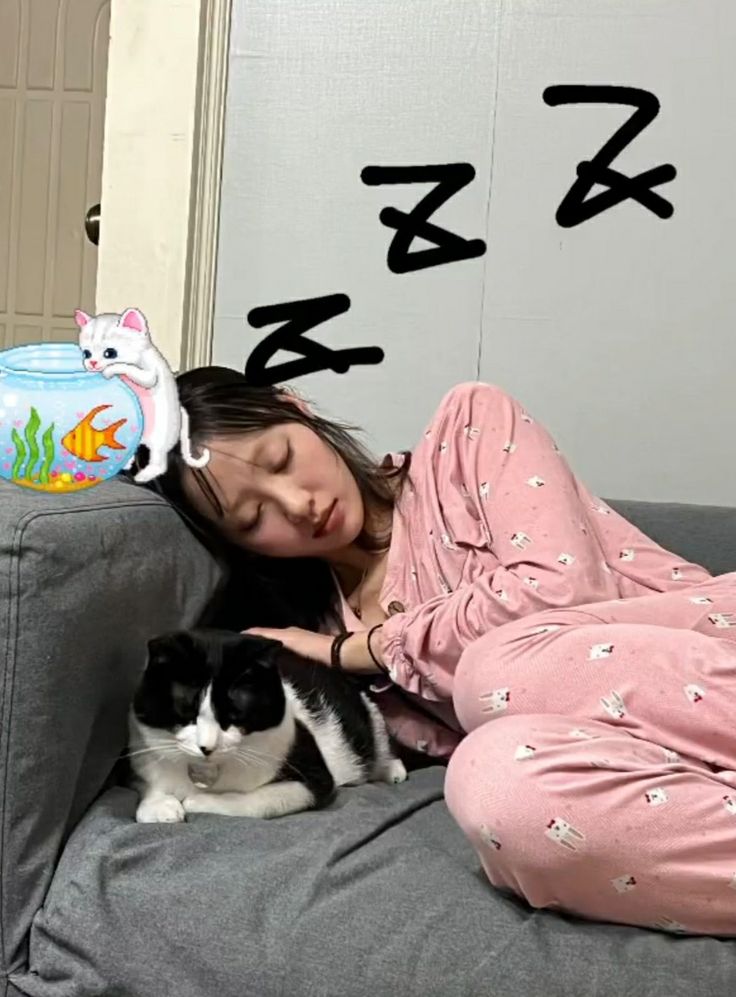 a woman laying on top of a gray couch next to a black and white cat